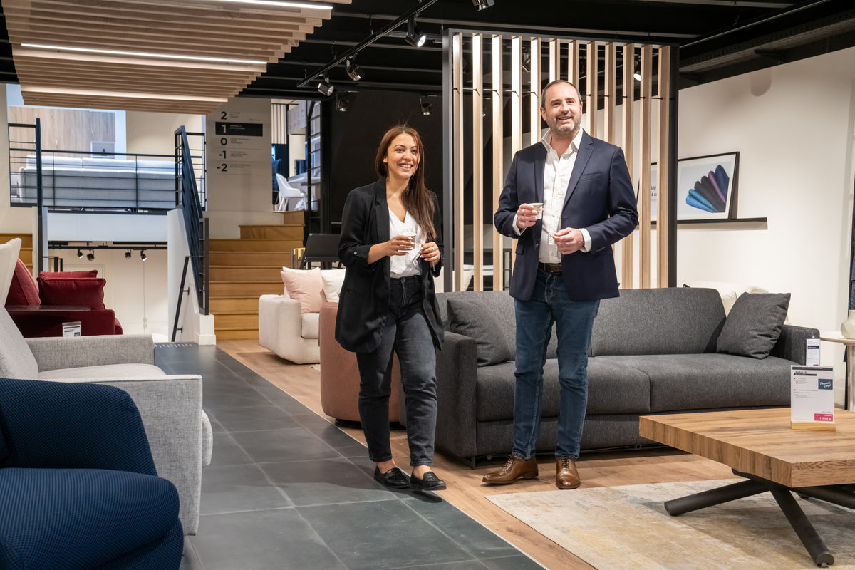 Deux personnes souriantes discutent dans un showroom de meubles modernes, entourées de canapés et de tables en bois