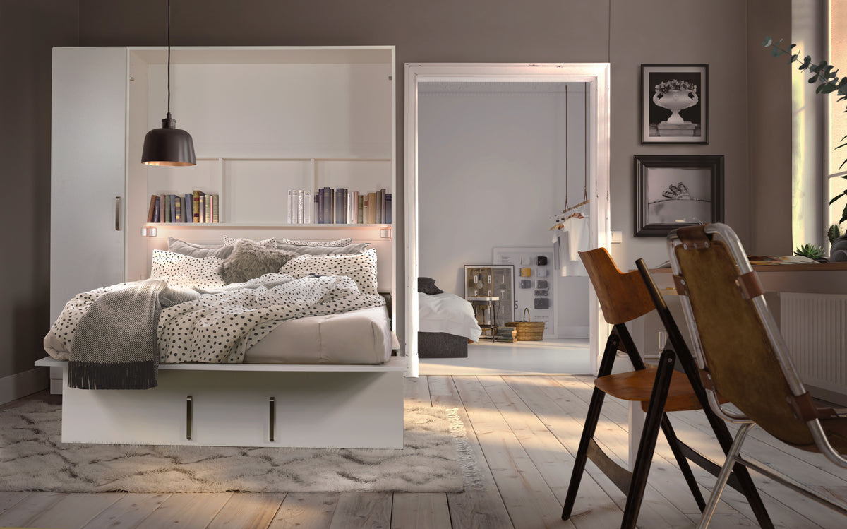 Lit escamotable blanc ouvert avec étagères intégrées, entouré de décor moderne et chaises en bois, dans une chambre lumineuse