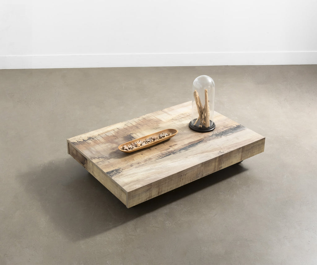 Table basse en BOSTON Mélaminé Morera avec finition bois naturel, décorée d'un plateau allongé et d'un objet décoratif sous cloche, posée sur un sol en béton lisse.