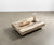 Table basse en BOSTON Mélaminé Morera avec finition bois naturel, décorée d'un plateau allongé et d'un objet décoratif sous cloche, posée sur un sol en béton lisse.