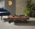 Table basse en CALYPSO Bois Massif Termotrattato avec plateau en bois massif thermotraité, ambiance moderne avec fauteuil bleu et plantes vertes dans un salon lumineux.