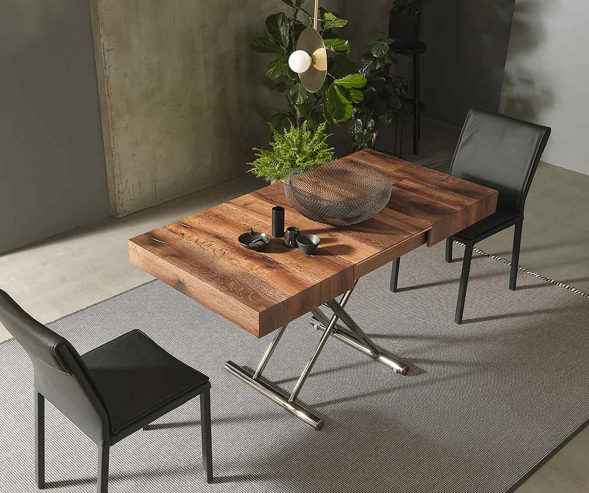 Table extensible en CALYPSO Bois Massif Termotrattato à finition bois naturel, avec piètement en métal design, accompagnée de deux chaises noires modernes dans un salon contemporain.