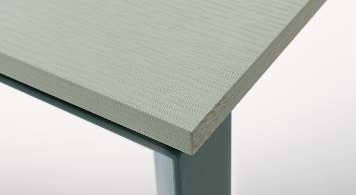 Gros plan sur le coin d'une table Domino M27 N48, finition amande, avec un plateau texturé et un pied en métal