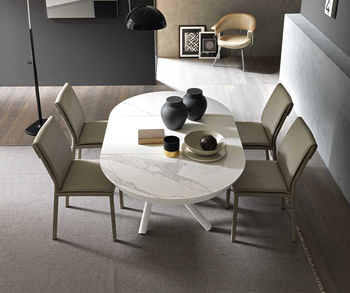 Table extensible moderne HELIOS Ceramique Brillante Blanc avec plateau en céramique blanche brillante, entourée de quatre chaises élégantes dans un intérieur contemporain.