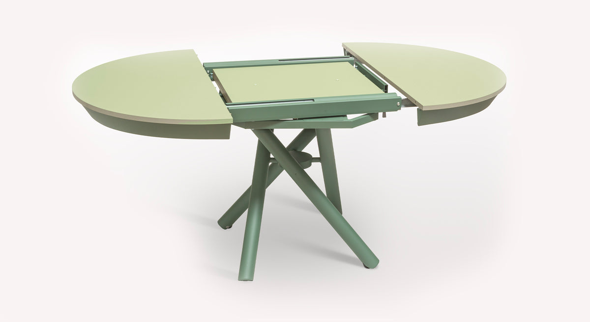 Table extensible Helios verte, avec plateau ovale ouvert et pieds croisés, montrant le mécanisme d'extension