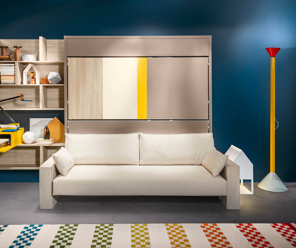 Canapé convertible moderne beige installé devant un mur bleu avec rangement mural coloré, illustrant le modèle KALI SOFA +50 coloris & matériaux, un canapé lit escamotable pratique et design.