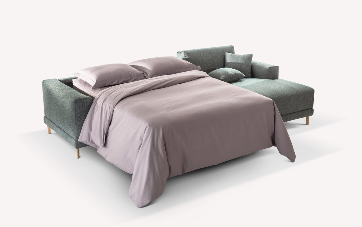 Canapé convertible gris en angle, ouvert en position lit avec draps gris clair et coussins assortis