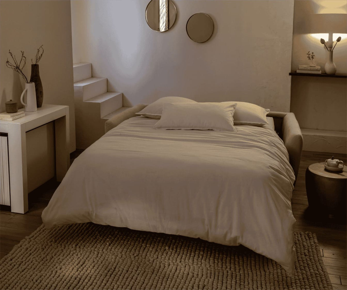 Canapé convertible BOW Mariclo Etain en tissu beige, déplié en lit double dans un salon chaleureux au design épuré avec tapis et décoration minimaliste.