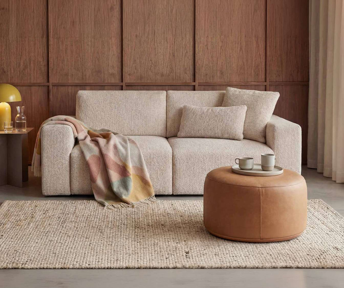 Canapé convertible DOLLY Fixe Silencio Ivoire en tissu beige clair, décoré d’un plaid coloré, avec coussins assortis dans un salon chaleureux au style moderne.
