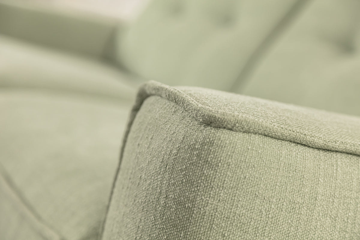 Gros plan sur l'accoudoir d'un canapé convertible en tissu vert eucalyptus, modèle Eddy