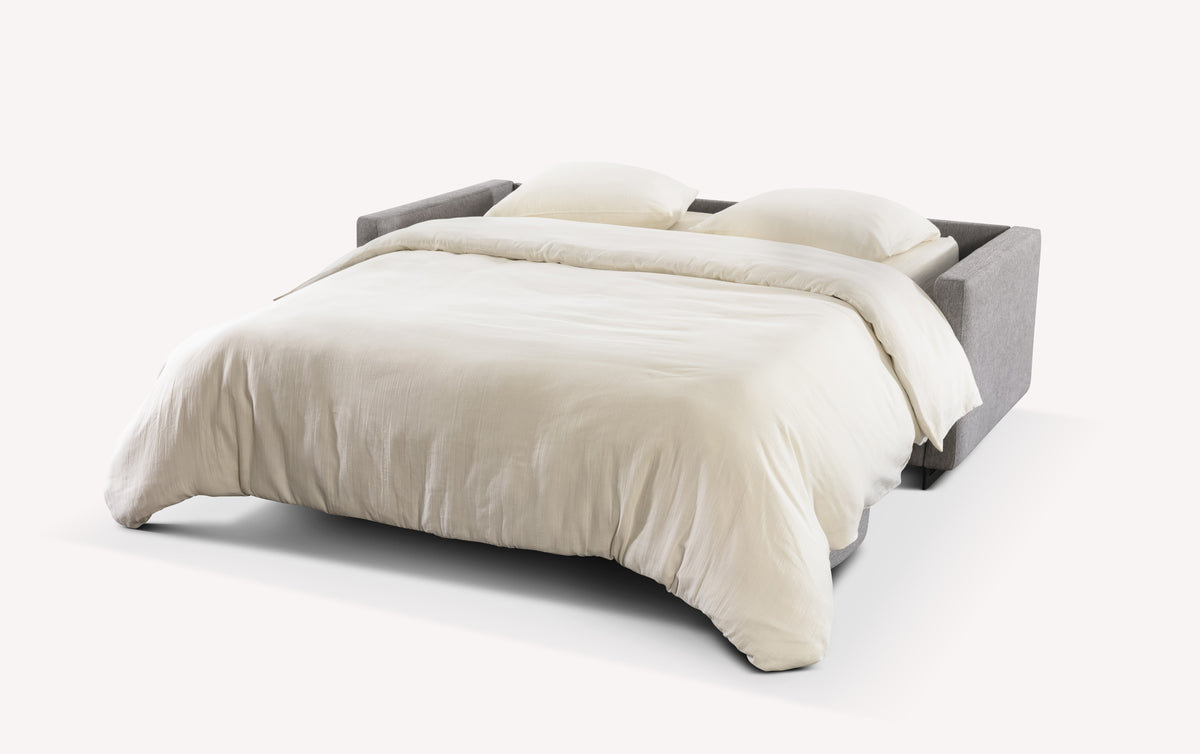 Lot canapé et pouf JUSTIN en mode lit, avec un couchage confortable et un revêtement gris, idéal pour un usage quotidien comme canapé convertible avec vrai matelas.