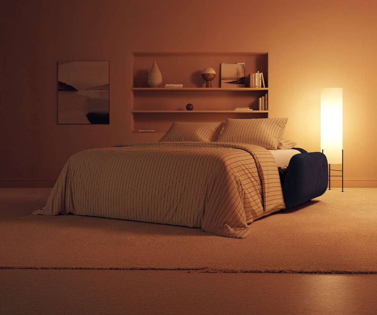 Canapé convertible MOON Moby Ocean dans une chambre chaleureuse avec lumière douce, linge de lit rayé beige et décoration minimaliste, parfait pour couchage quotidien.