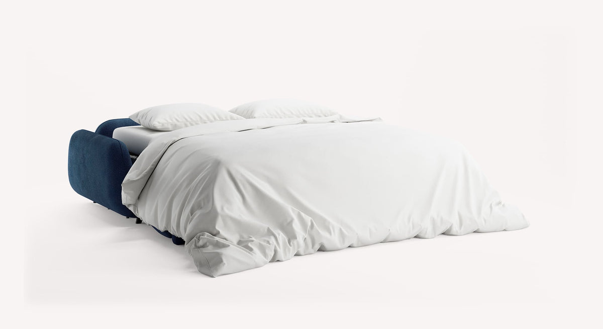 Canapé convertible MOON Moby Ocean en velours bleu océan avec couchage déplié, literie blanche et deux oreillers, conçu pour un couchage quotidien confortable.