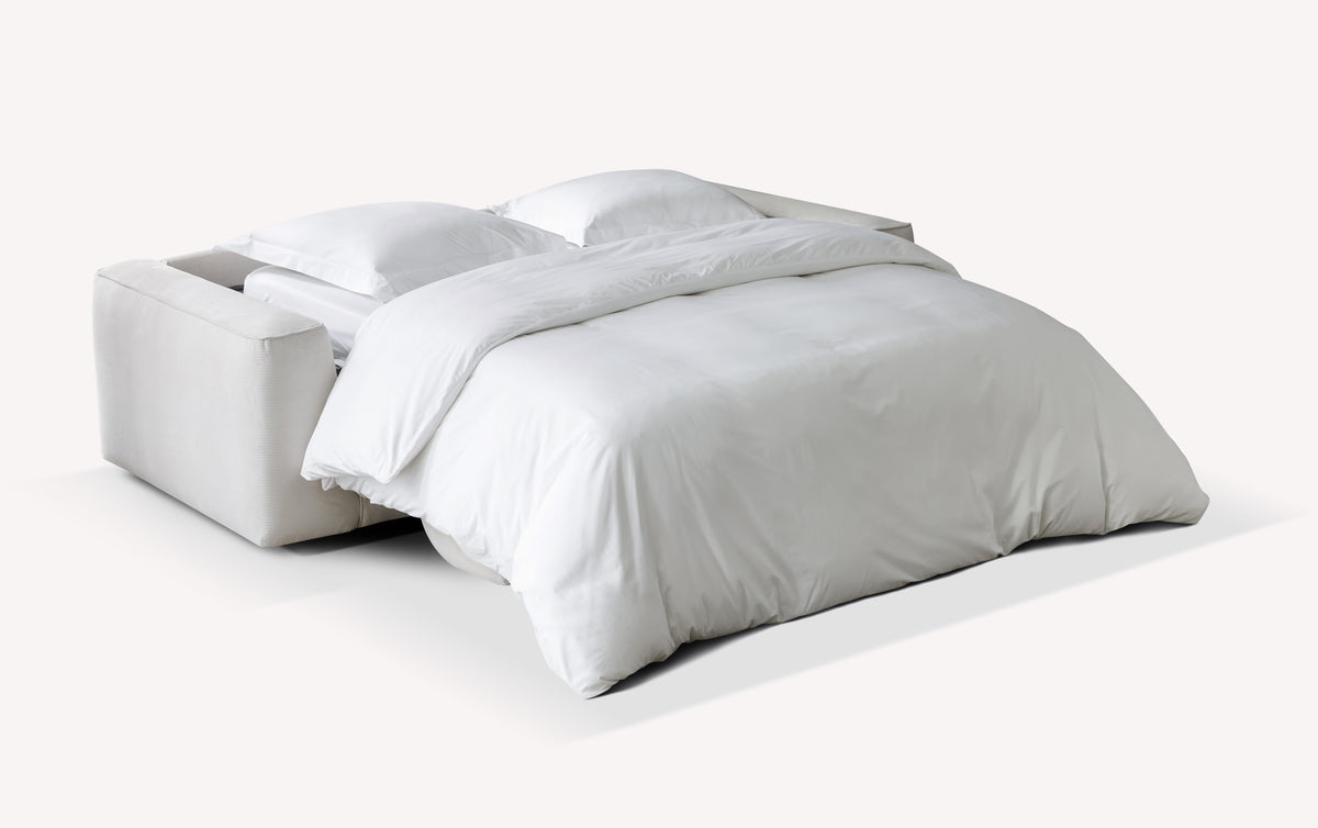 Lot canapé et pouf ONYX Teatro Sand en velours côtelé beige clair transformé en canapé convertible avec un couchage spacieux habillé de linge de lit blanc.