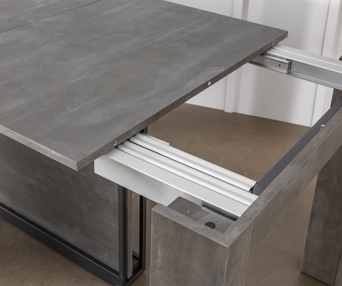 Table extensible en finition pierre grise avec mécanisme métallique visible, modèle COMPACT Mélaminé Pietra, idéal pour optimiser l’espace et accueillir plusieurs convives.