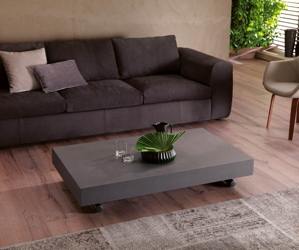 Table basse moderne MÉLANGE Mélaminé Béton gris mat posée sur roulettes devant un canapé élégant dans un salon lumineux au style épuré.