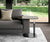 Table d'appoint avec plateau en SERVUS Verre Marbré Sahara noir lucido, posée à côté d'un canapé gris dans un salon contemporain avec vue sur jardin.