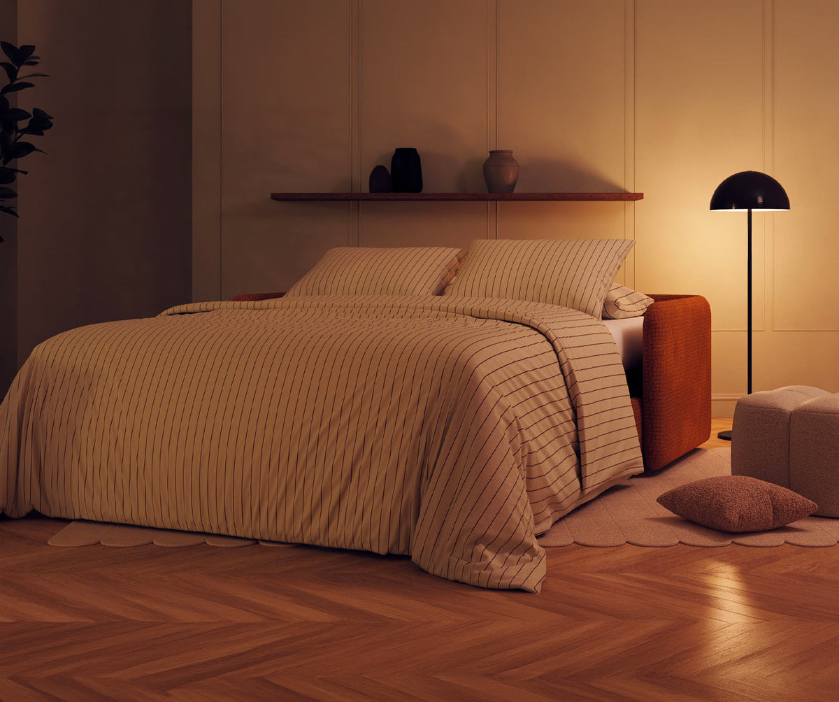 Canapé convertible ARLO Paradoxe Cuivre dans une chambre chaleureuse avec éclairage tamisé, mettant en valeur un canapé BZ au revêtement cuivre et un décor sobre et élégant.