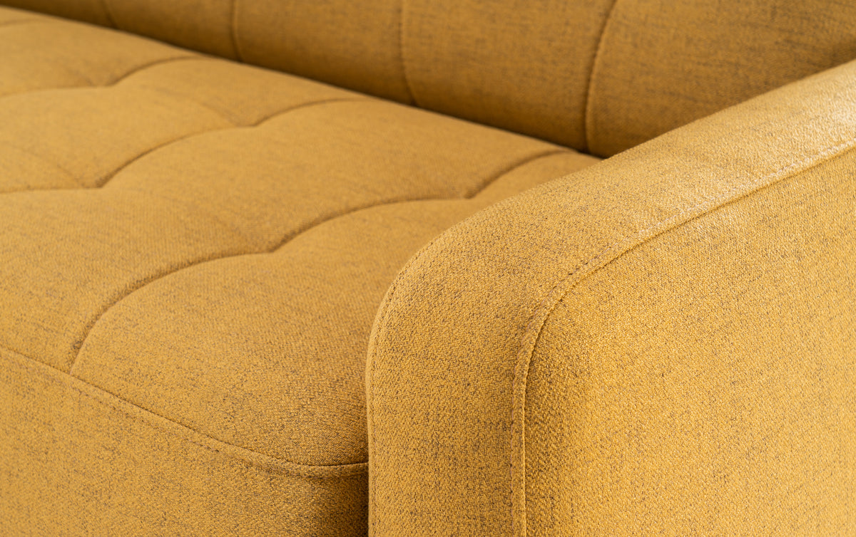 Détail en gros plan de l'accoudoir et de l'assise en tissu jaune moutarde du canapé convertible CLARK Fixe Foster Curcuma, offrant une texture douce et un design moderne.