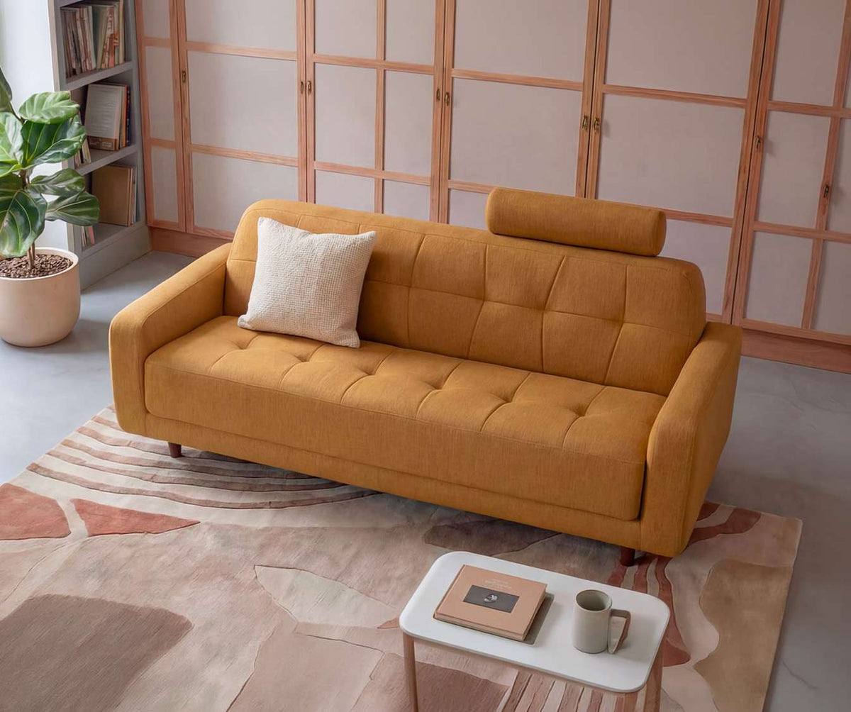 Canapé convertible CLARK Fixe Foster Curcuma en tissu jaune safran avec appuie-tête, présenté dans un salon lumineux avec coussin beige et décoration moderne.