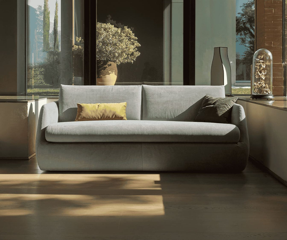 Canapé convertible LUZ Foster Silver en tissu gris clair avec coussins décoratifs, installé dans un salon lumineux et moderne, idéal pour couchage quotidien.