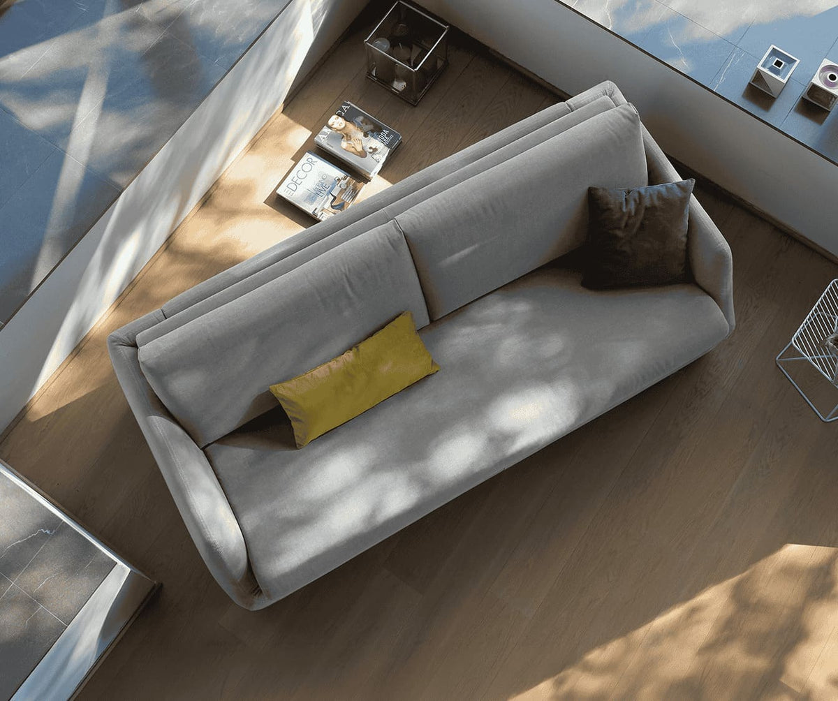 Canapé convertible LUZ Foster Silver en tissu gris clair, éclairé par une lumière naturelle, avec coussins décoratifs et ambiance moderne épurée.