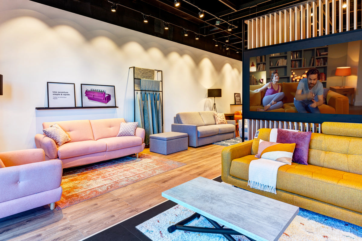 Showroom de La Maison du Convertible avec canapés colorés, table basse moderne et affiches promotionnelles. Ambiance chaleureuse et design