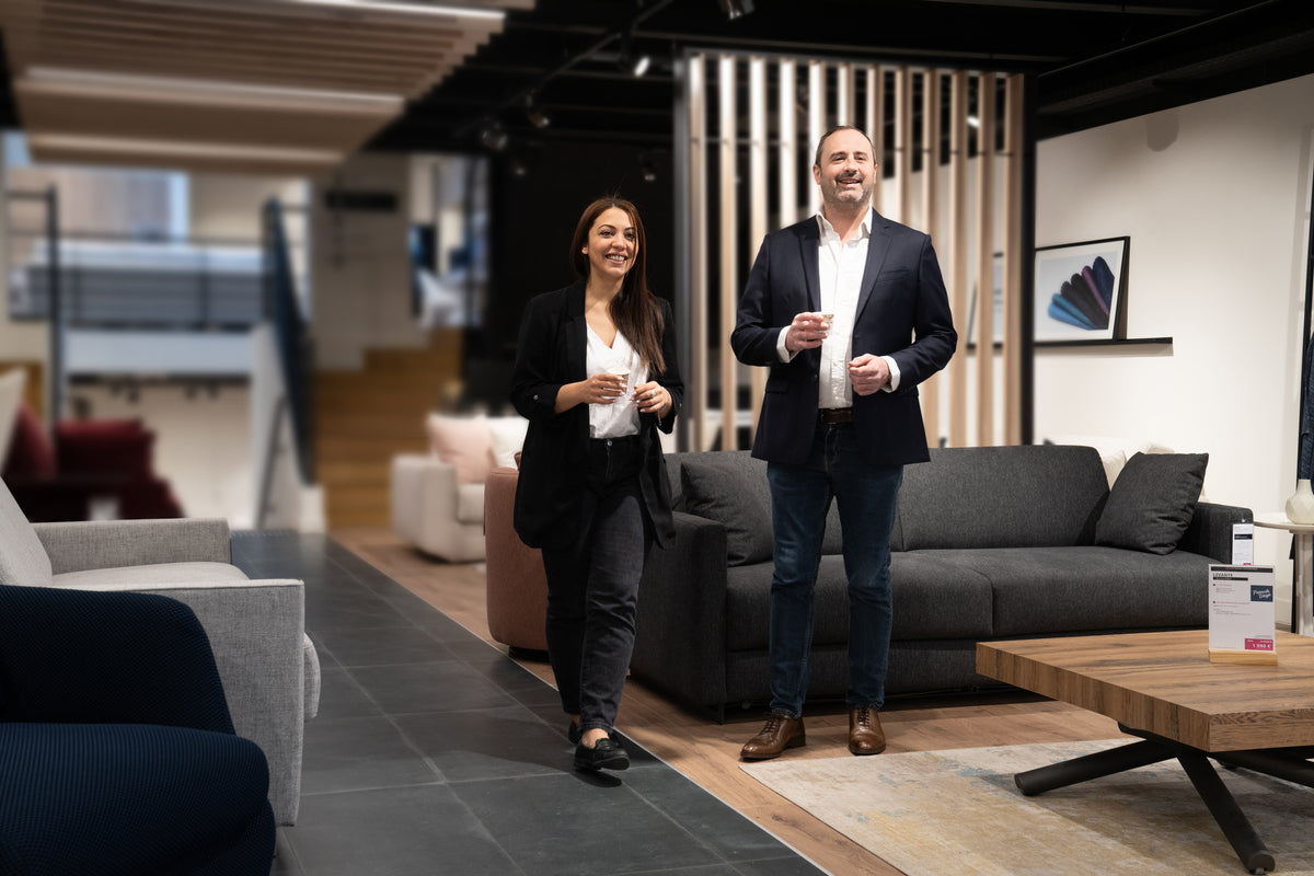Deux personnes souriantes dans un showroom de meubles modernes, probablement à "La Maison Convertible" au 85 avenue Victor Hugo