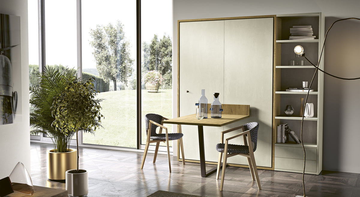 Salle à manger moderne avec table pliante intégrée à un lit escamotable, entourée de chaises et d'étagères, vue sur jardin