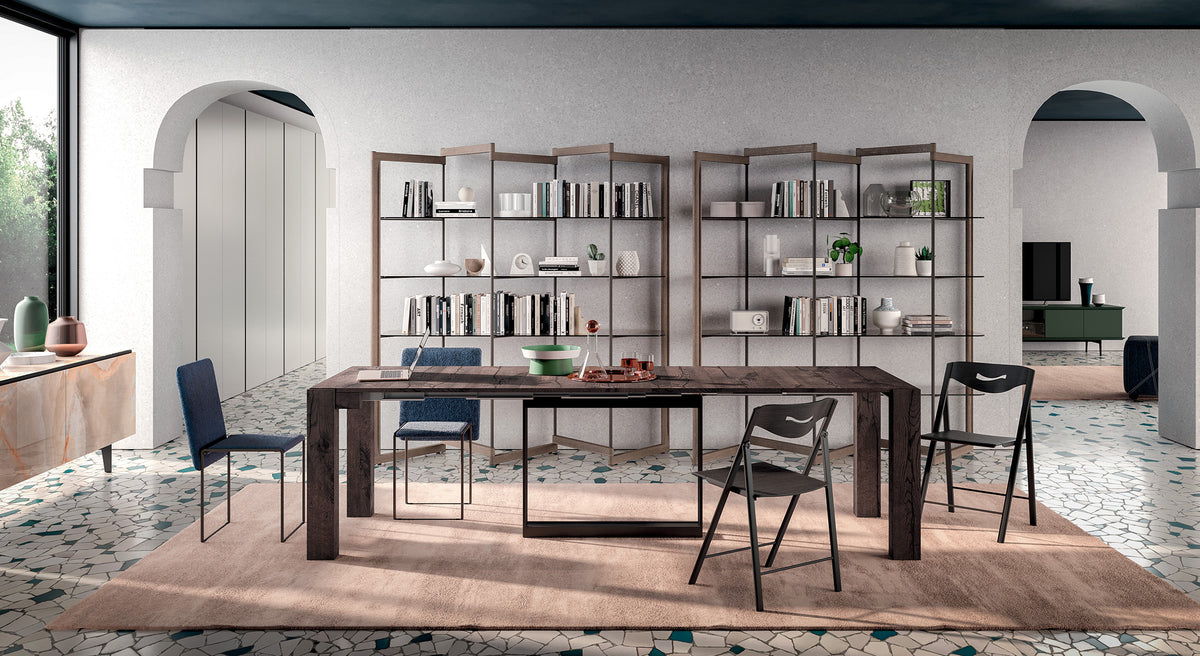 Table extensible en bois foncé ouverte, entourée de chaises dans une pièce moderne avec étagères remplies de livres et objets décoratifs