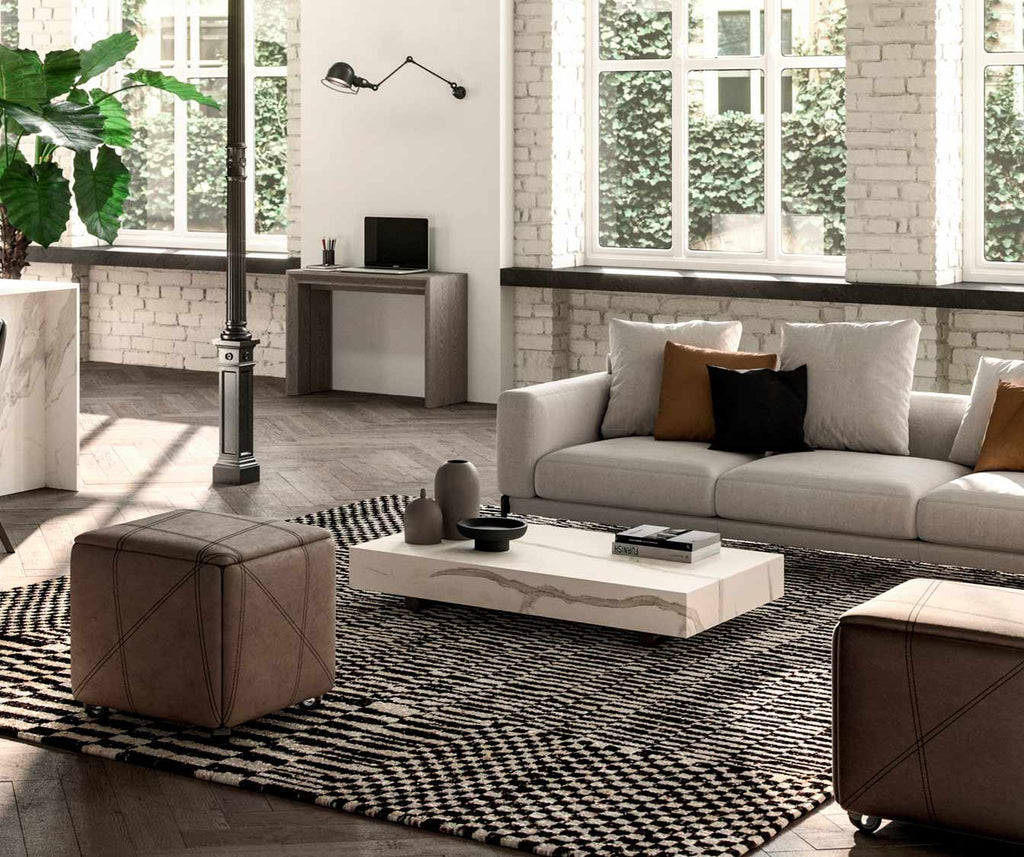 Salon lumineux avec canapé et poufs en cuir, table basse blanche posée sur un tapis graphique, mettant en valeur l'élégance du BOX Verre Extrachiaro dans un intérieur moderne.