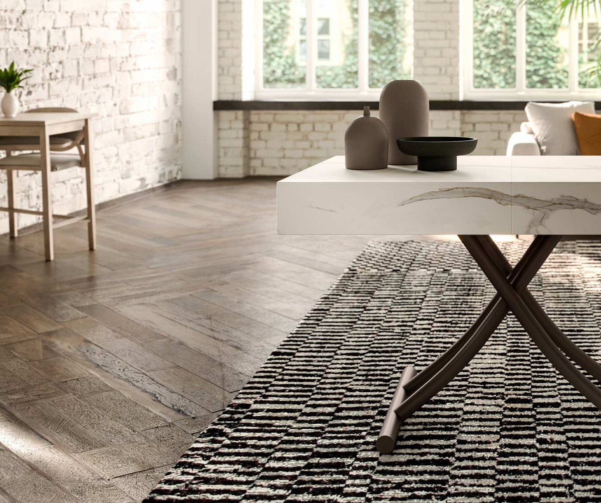 Table extensible moderne avec plateau en BOX Verre Extrachiaro posé sur un tapis à motifs géométriques dans un salon lumineux au sol en parquet bois.