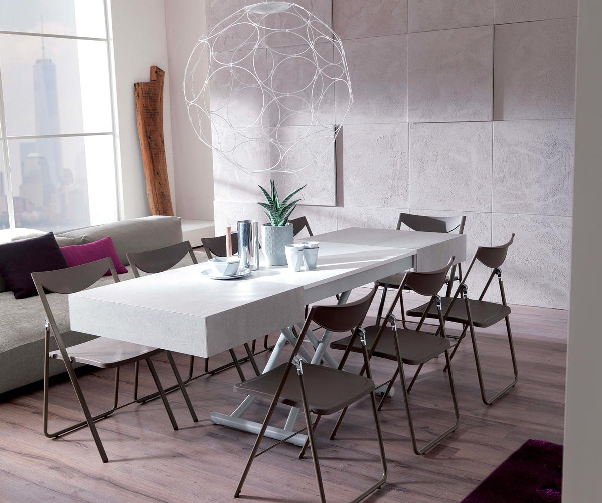 Table extensible moderne avec plateau blanc laqué dans un salon lumineux, mise en scène avec six chaises pliantes, design épuré, modèle BOX Verre Extrachiaro.