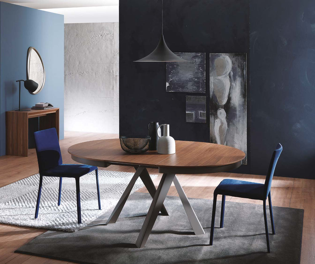 Salle à manger moderne avec table extensible en bois et métal EMISFERO Verre Extrachiaro, deux chaises bleu marine, luminaire suspendu et décoration murale contemporaine.