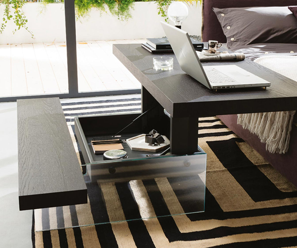 Table extensible moderne en MARKUS Plaqué Rovere vecchio naturale avec plateau en bois foncé et base en verre transparent, intégrant un espace de rangement pratique sous le dessus.