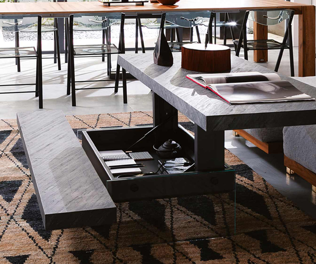 Table basse moderne avec rangement intégré ouverte, finition MARKUS Plaqué Rovere vecchio naturale, posée sur un tapis à motifs géométriques dans un salon lumineux.