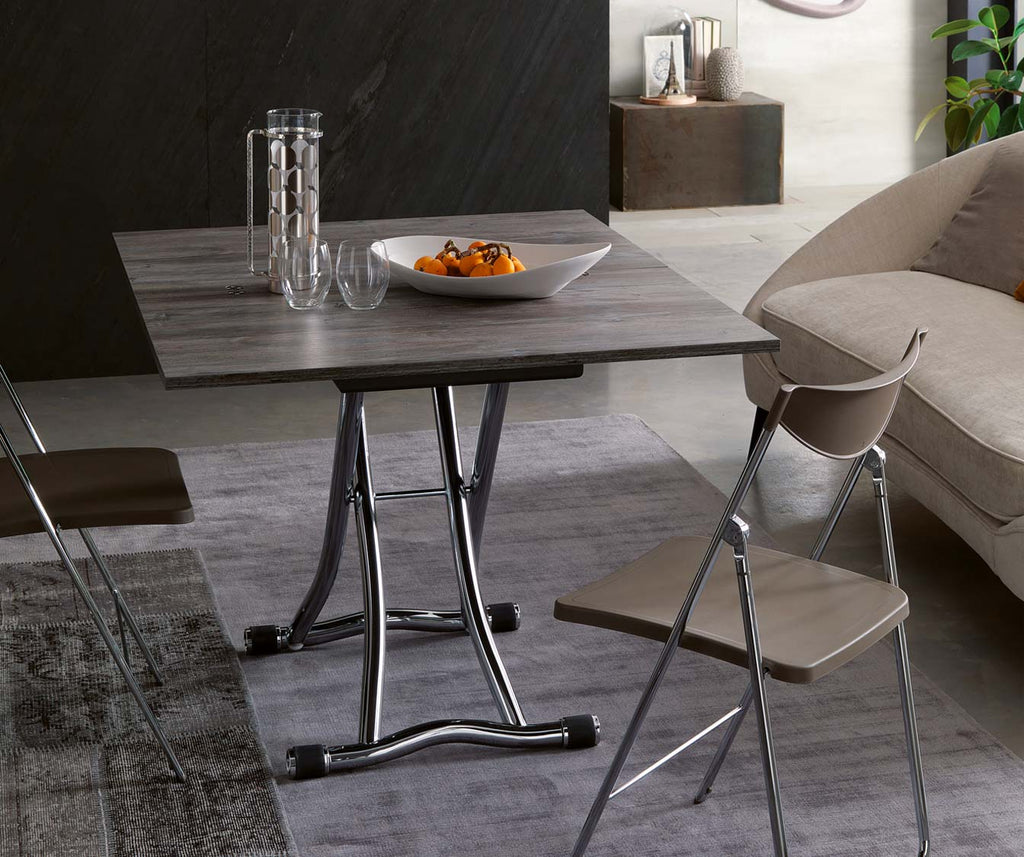 Table extensible SYDNEY Mélaminé Ancien cendré avec plateau en bois gris et pieds métalliques, aménagée dans un salon moderne avec chaises pliantes et canapé beige.