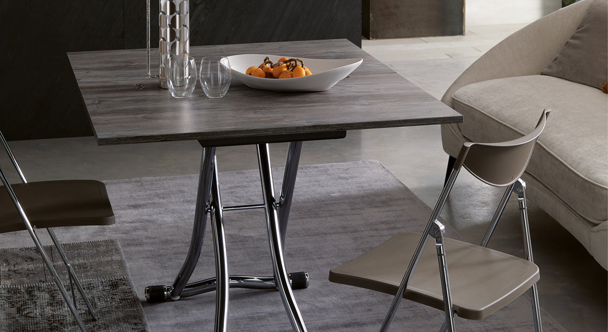 Table extensible moderne ouverte avec plateau en bois, entourée de chaises pliantes et d'un canapé, décorée d'un plat de fruits