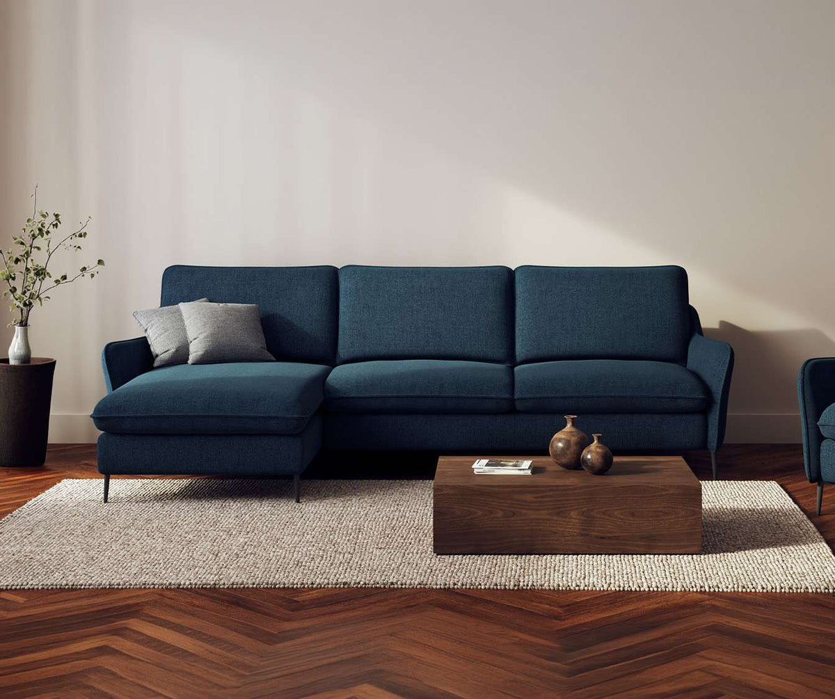 Canapé d'angle BOGART Angle Foster Bleu ocean en tissu bleu océan avec coffre de rangement, dans un salon moderne et épuré avec table basse en bois et tapis beige.