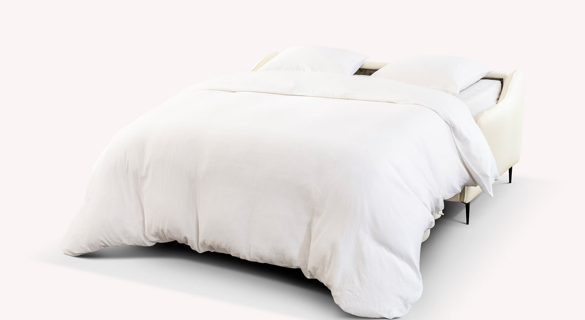 Canapé convertible Bogart en cuir crème, ouvert en position lit avec draps blancs