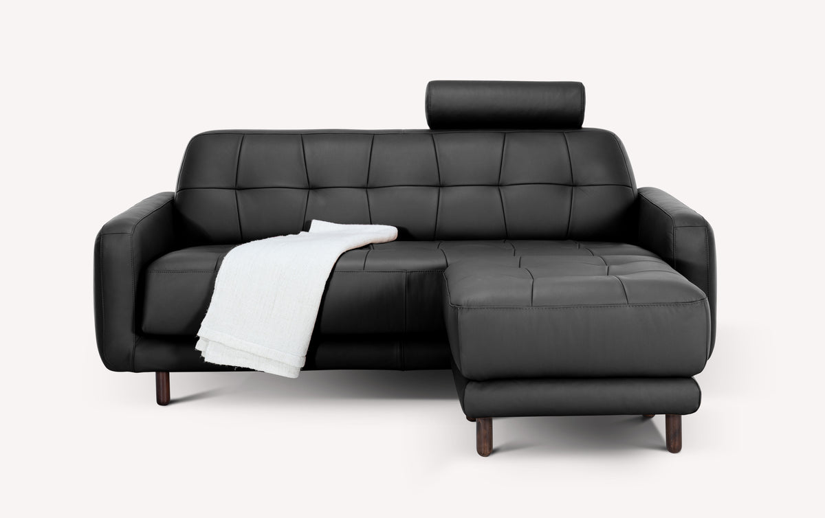 Lot canapé et pouf CLARK Cuir Sidney Noir en cuir noir élégant avec assise modulable, coussin d'appui-tête et plaid blanc, design moderne et confortable.