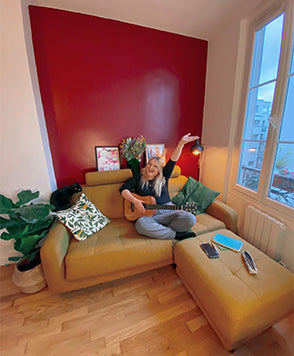 Jeune femme souriante avec une guitare sur canapé-lit CLARK jaune dans un salon, avec pouf assorti