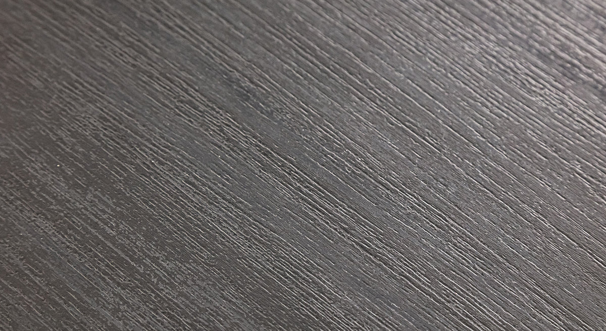 Surface texturée gris foncé avec des stries parallèles, évoquant un matériau moderne et élégant