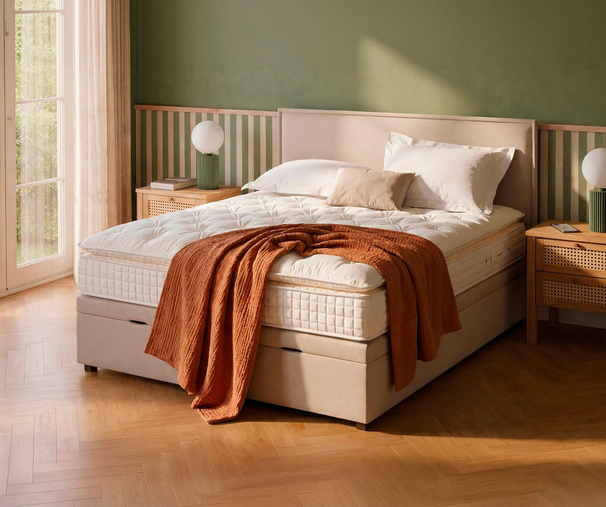 Lit coffre OUESSANT Luca Beige dans une chambre lumineuse avec parquet en bois clair, habillé de linge de lit blanc et d'un plaid marron, pour un couchage confortable et élégant.