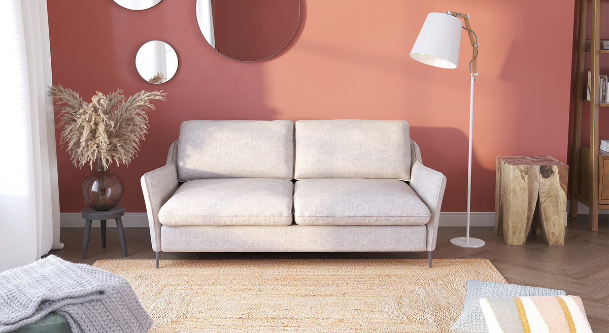 Canapé convertible BOGART Foster Silver dans un salon lumineux avec mur terracotta, tapis naturel, lampe blanche et décoration épurée pour un couchage quotidien confortable.