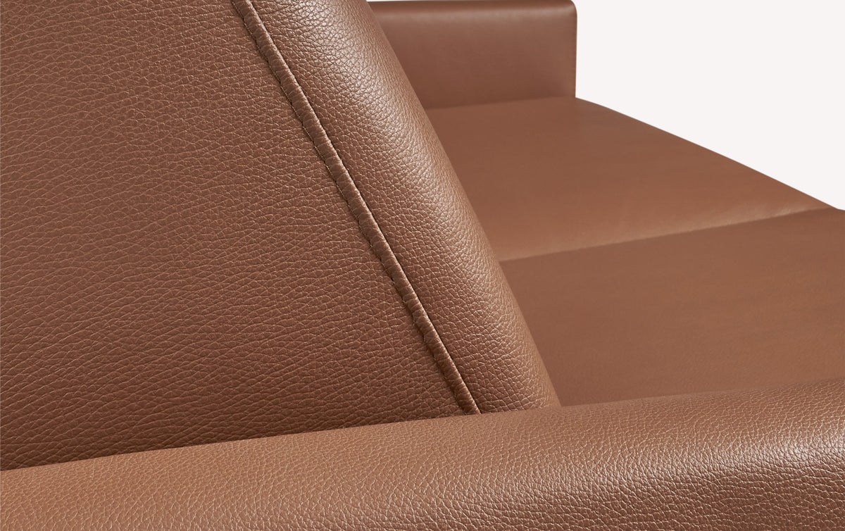 Gros plan sur le tissu en cuir cognac luxueux d'un canapé convertible Bobby, montrant la revêtement et les coutures détaillées