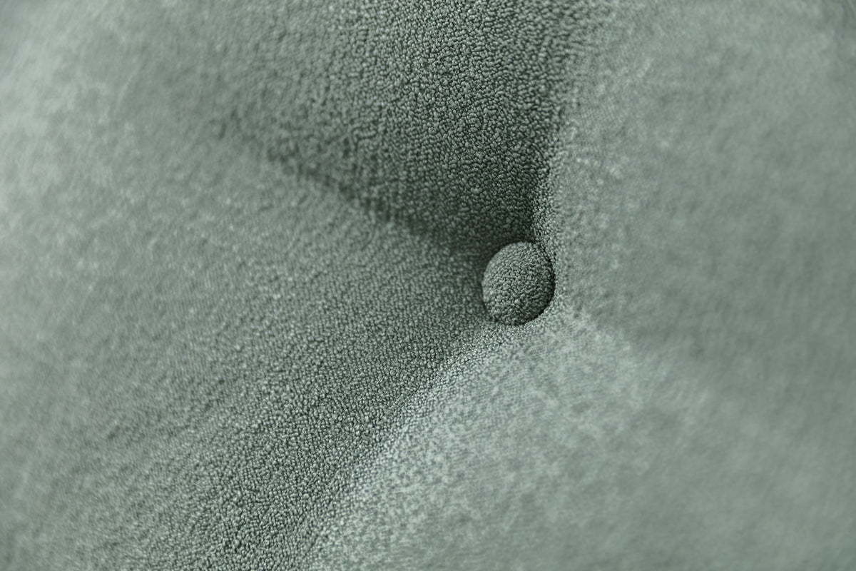 Gros plan sur le tissu texturé vert eucalyptus du canapé convertible Finn, avec un bouton central