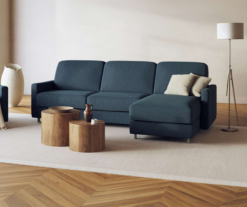 Canapé JIMMY Angle Foster Bleu ocean en tissu bleu océan, avec méridienne à droite, décoré de coussins clairs, dans un salon au sol parquet et tapis beige, avec tables basses en bois.