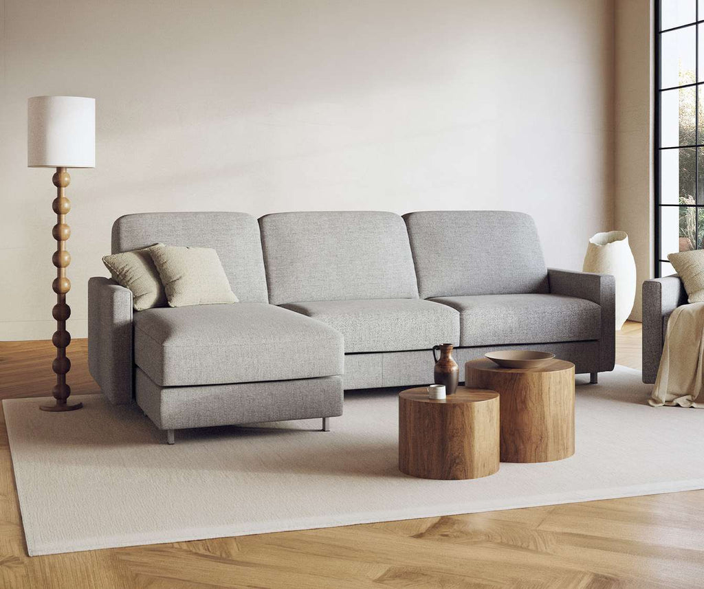 Canapé convertible JIMMY Angle Foster Grey en tissu gris clair avec méridienne, idéal pour un couchage quotidien, dans un salon lumineux et minimaliste avec lampadaire bois et tables basses rondes.