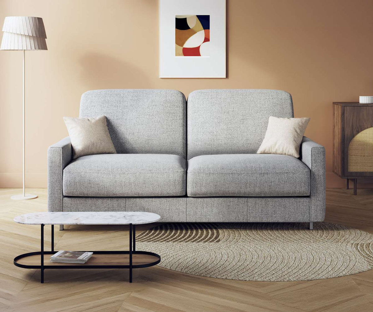 Canapé convertible JIMMY Foster Grey en tissu gris clair, style moderne et épuré, disposé dans un salon avec décoration chaleureuse et table basse ovale noir et blanc.